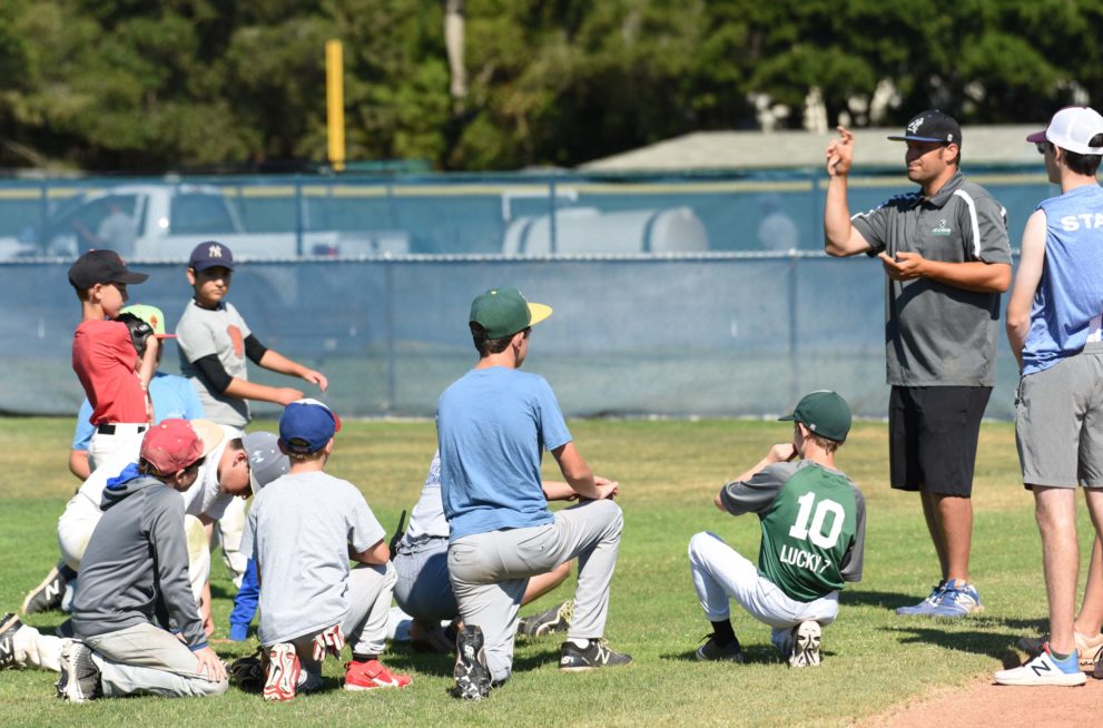 Campers in baseball gear huddling around with their coach.