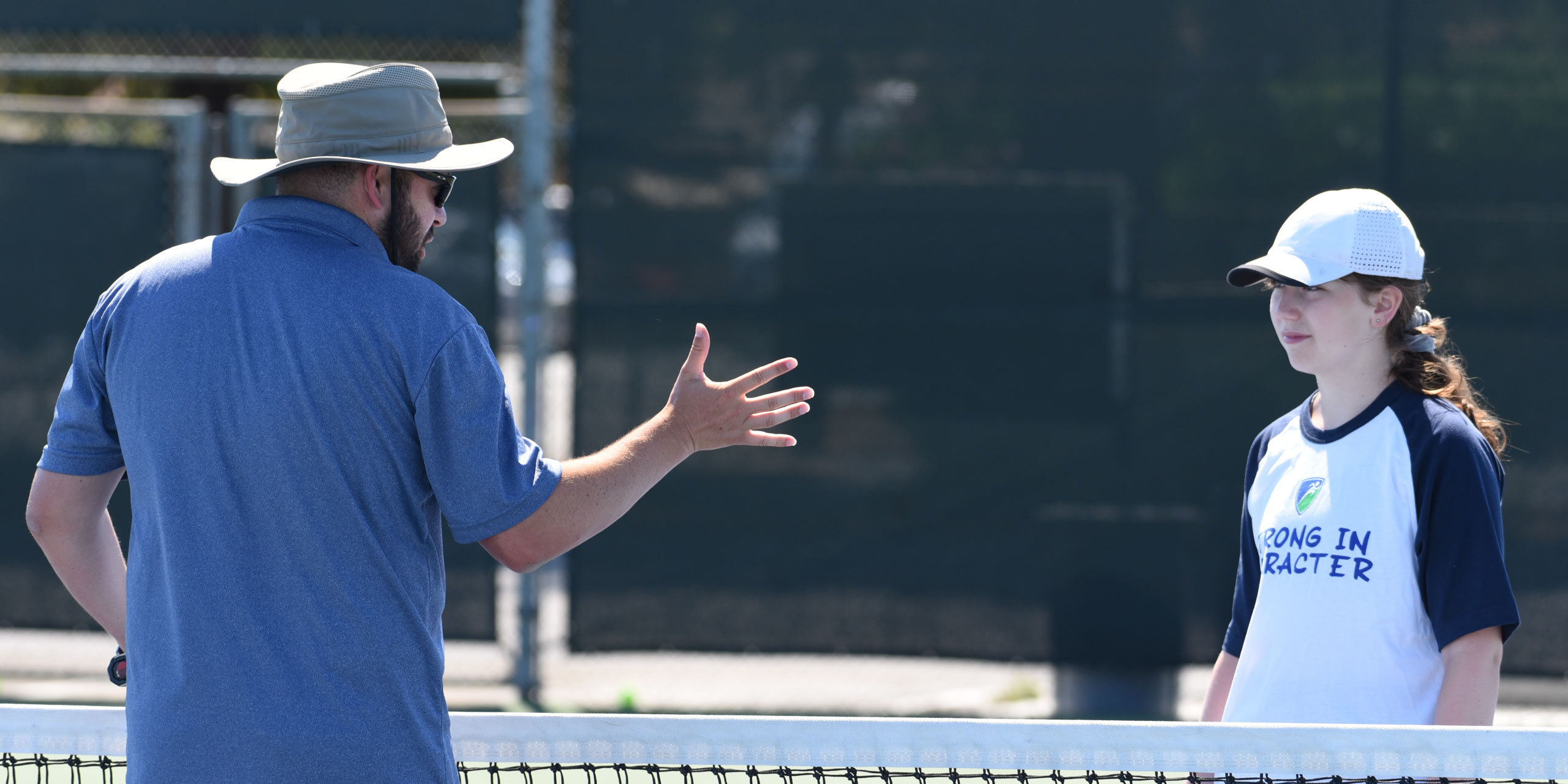 A coach teaching tennis to a camper.
